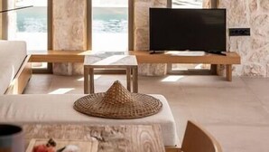 Una habitación con pared de piedra, un televisor sobre un atril de madera, una cesta tejida y una mesa con comida.