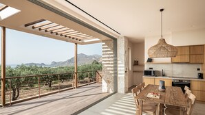 En rummelig balkon med udsigt til bjerge og et træbord med stole.