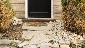 Een houten huis met een zwarte deur, een decoratieve krans en een pad van stenen dat naar de ingang leidt.