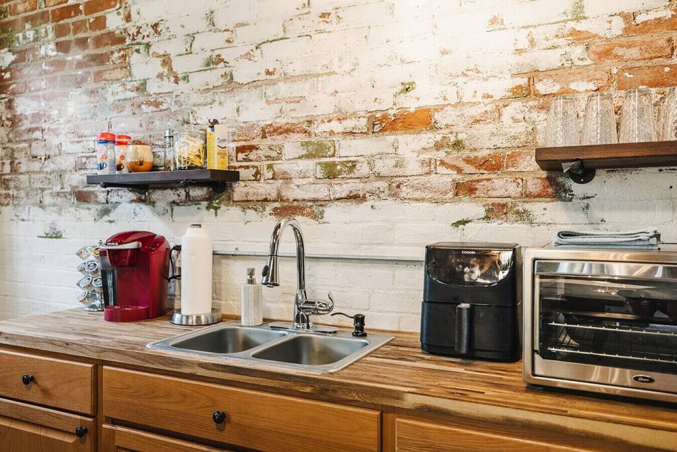 Une cuisine avec un mur en briques au style rustique, un évier à deux bacs, une machine à café, un grille-pain et une étagère remplie de bocaux.