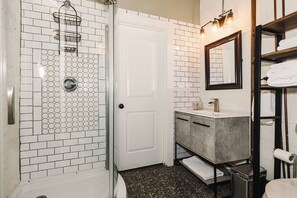Un baño con ducha, lavamanos, espejo y toallero.