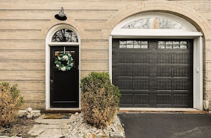 A building with a brick facade, a black door with a wreath, and a large garage door.