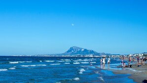 A beach with waves, people, and a mountain in the background.