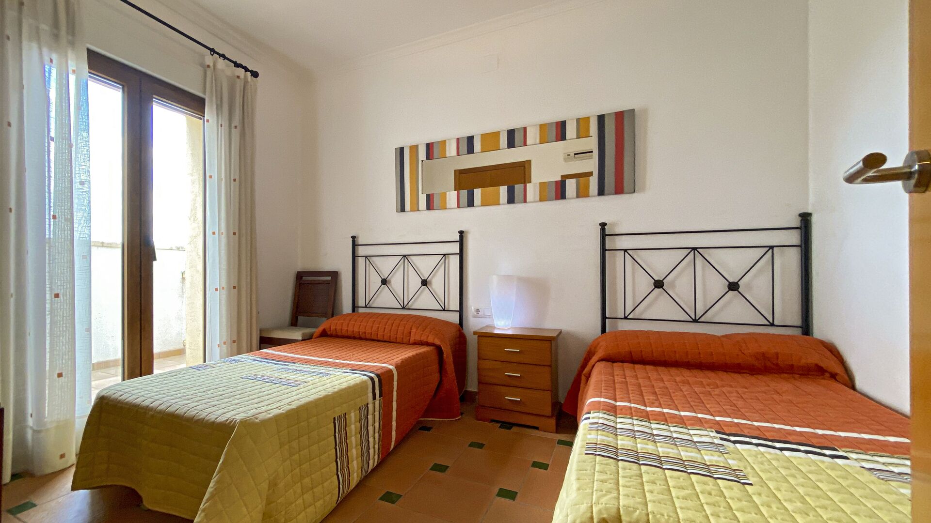 A room with two beds, a nightstand, a lamp, and a window with curtains.