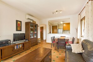 Een woonkamer met een televisie, een houten kast en een eethoek met stoelen en een tafel.