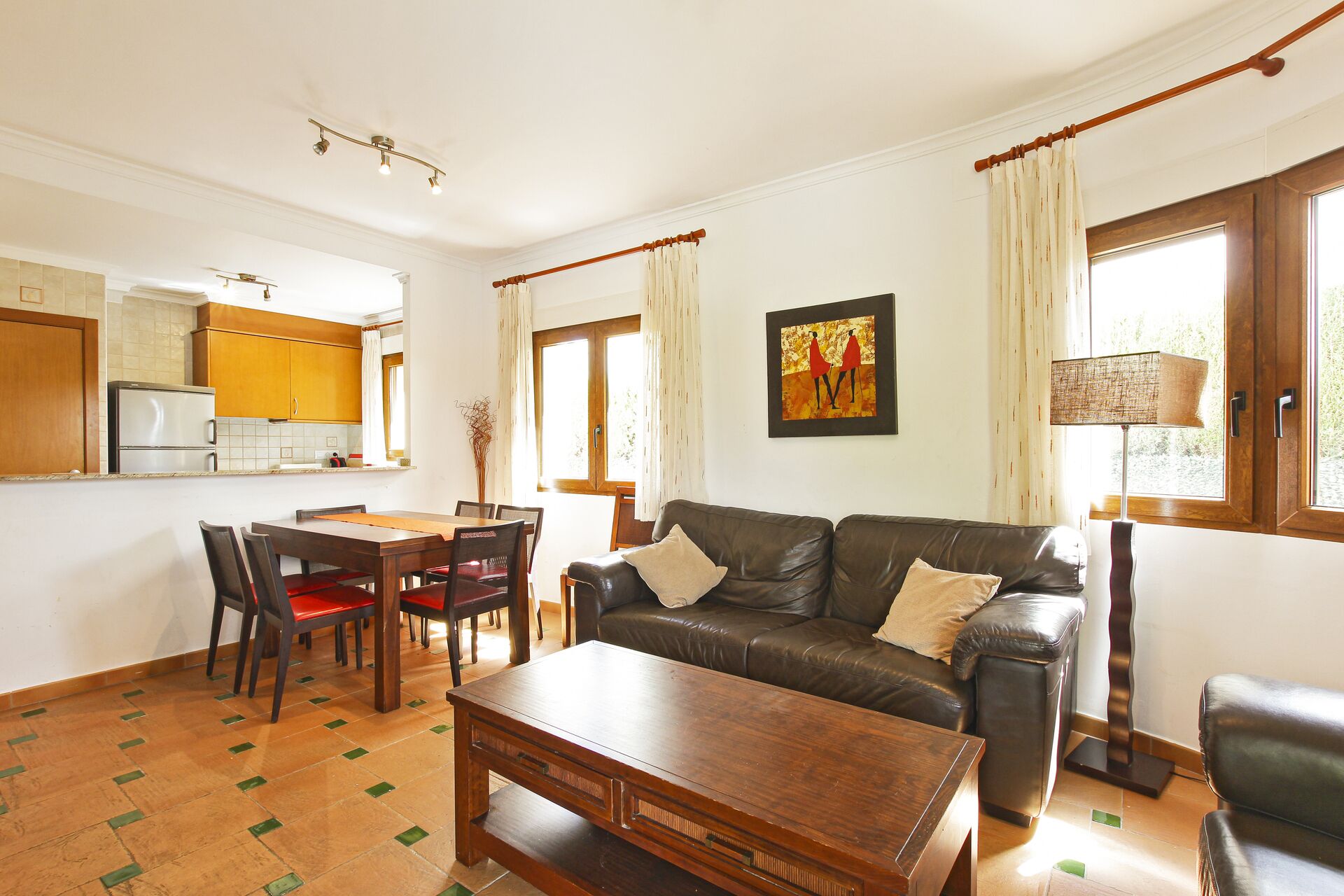 Una sala de estar con un sofá de cuero marrón, una mesa de centro de madera y un comedor con una mesa y sillas de madera.