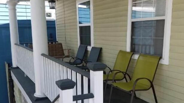 A covered porch with a white railing, two chairs, and a lantern.