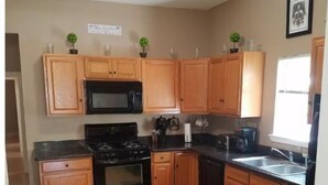 A kitchen with wooden cabinets, a black stove, a microwave, and a sink.