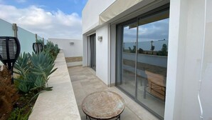 Un patio moderno al aire libre con una puerta de cristal que da a una terraza, rodeado de plantas y una pequeña mesa redonda.