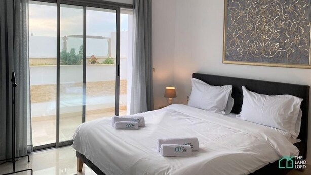 Habitación de hotel con una cama grande, vistas al exterior a través de una puerta corrediza de vidrio y un cuadro en la pared.