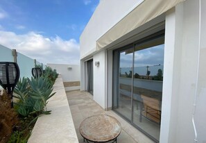 Un patio extérieur moderne, doté d’une porte vitrée donnant sur une terrasse, le tout agrémenté de plantes et d’une petite table ronde.