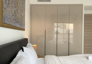 Ein Hotelzimmer mit Bett, grauem Kopfteil, Schrank und einem Gemälde an der Wand.