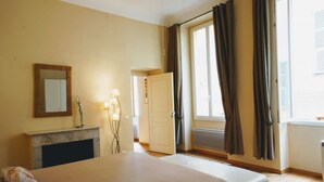 Une chambre à coucher avec un lit, une commode, un miroir, une lampe et une fenêtre avec des rideaux.