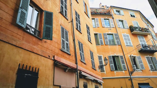Un immeuble à plusieurs étages, doté d’une façade jaune, de nombreuses fenêtres avec volets et d’une devanture visible au niveau du rez-de-chaussée.