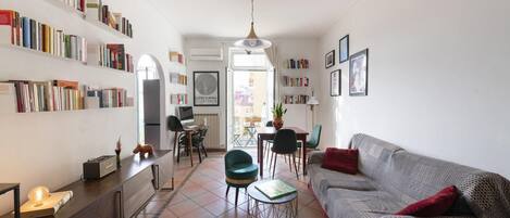 A living room with a sofa, a dining table, and a bookshelf filled with books.