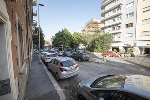 Une rue bordée de voitures garées et d’immeubles, dont un bâtiment commercial dont l’enseigne est visible.