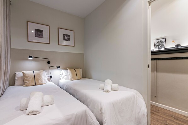 A hotel room with two beds, each with neatly folded towels, a bedside lamp, and framed pictures on the wall.