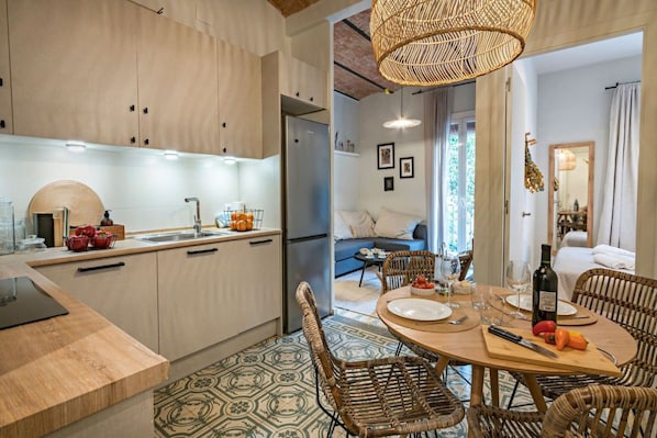 A modern kitchen with wooden cabinets, a dining area with wicker chairs, and a view into a living room.
