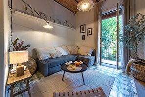 A cozy living room with a sofa, a coffee table with breakfast items, a lamp, and a view of greenery outside.