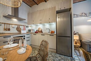 A modern kitchen with a dining area, stainless steel appliances, and a wicker chair.