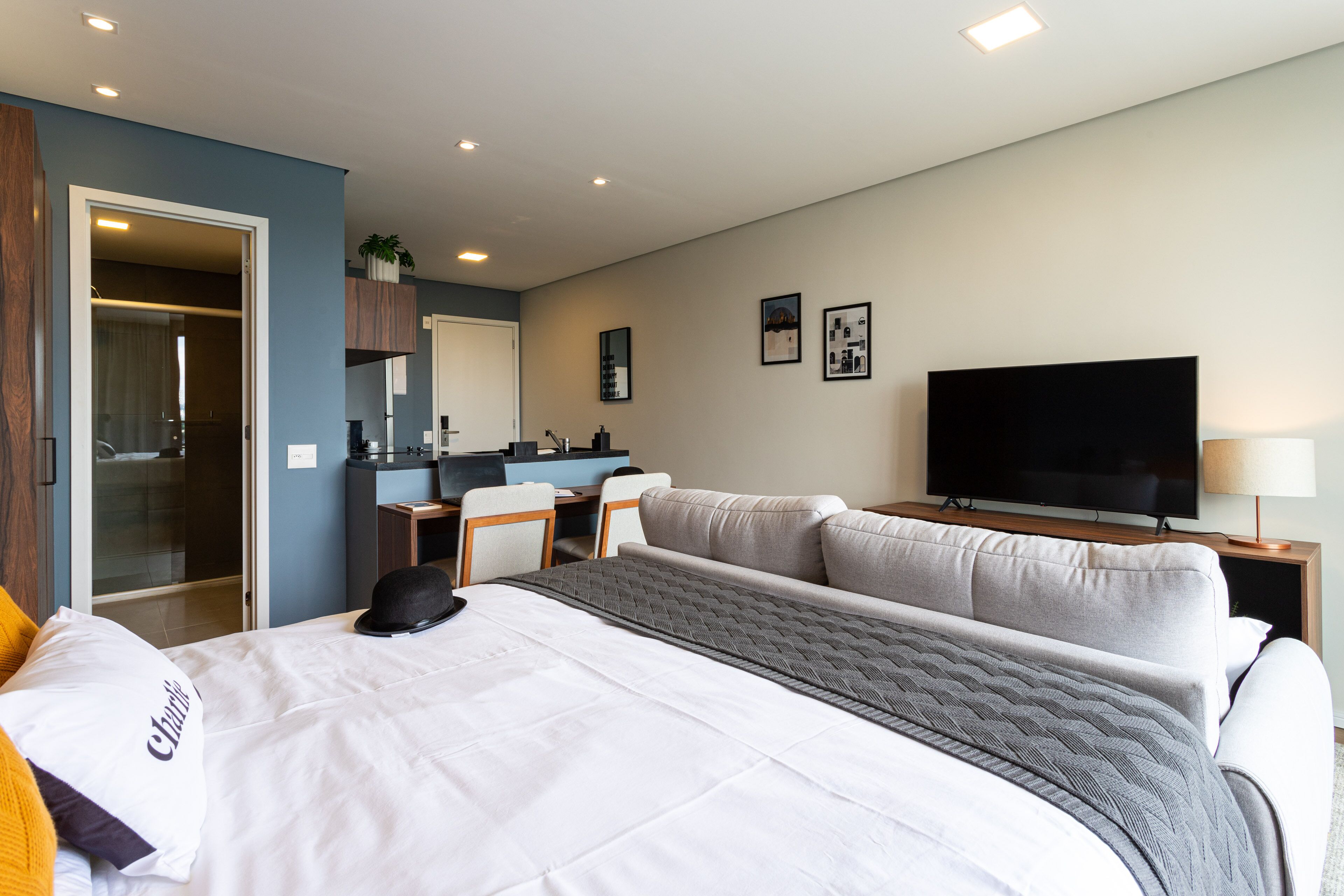 A hotel room with a bed, a TV, a desk, and a kitchenette.
