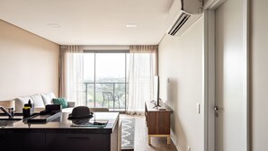 A modern hotel room with a large window, a desk with a computer, a chair, and a small table.
