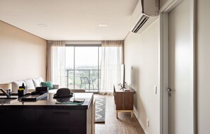 Een moderne hotelkamer met een groot raam, een bureau met een computer, een stoel en een kleine tafel.