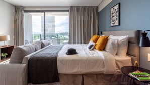 A modern hotel room with a large bed, a sofa, a desk, and a view of the cityscape.