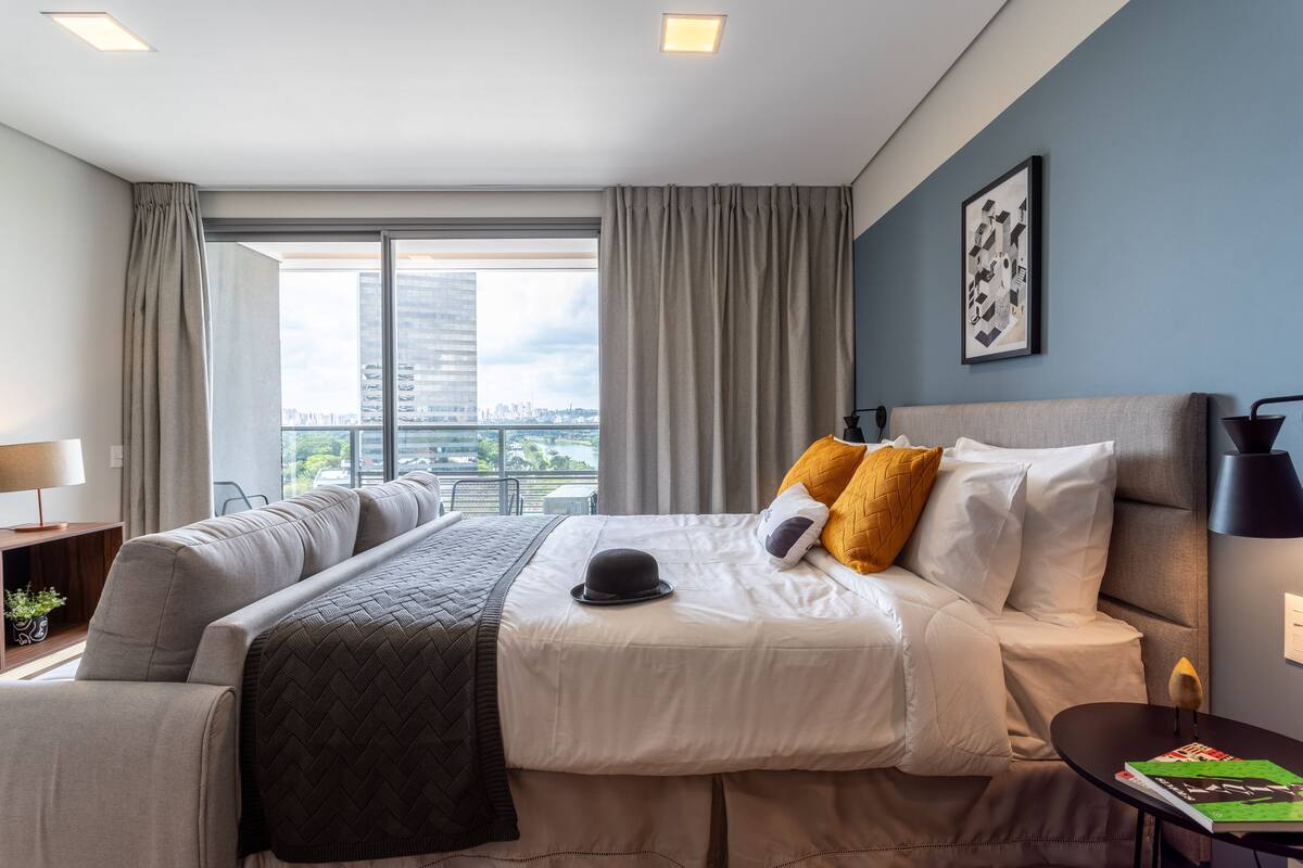 A modern hotel room with a large bed, a sofa, a desk, and a view of the cityscape.