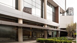 A modern building with large windows, a central atrium, and a landscaped area with grass and trees.