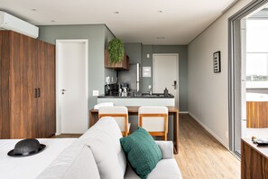 Eine moderne Wohnung mit Küchenzeile, Essbereich und Wohnzimmer mit Sofa und einem Hut auf dem Bett.