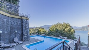 A swimming pool with lounge chairs, a stone wall, and a view of a lake and mountains. - casa_andrea_varenna_varennaholidays (Perledo)