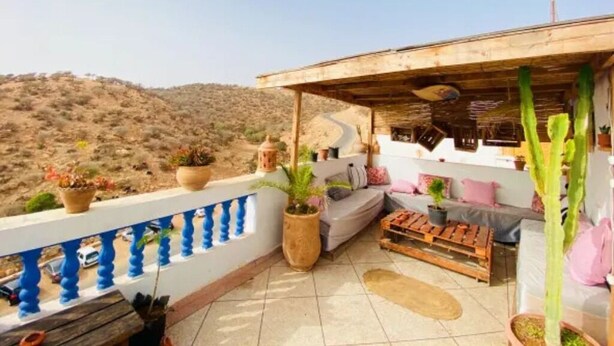 Terraço no telhado com sofá, mesa de madeira e plantas em vasos.