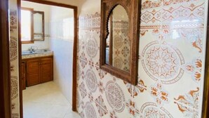 Um corredor com azulejos estampados, um espelho com moldura de madeira e um relógio na parede.