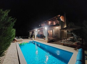 Ein zweigeschossiges Haus mit Swimmingpool, Gartenmöbeln und einer überdachten Terrasse.