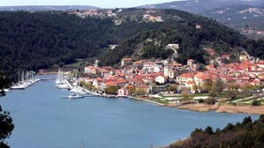 Eine Küstenstadt mit einem Hafen, Gebäuden mit roten Dächern und hügeliger Landschaft im Hintergrund.