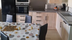 A compact kitchen with a refrigerator, microwave, oven, and sink. There is a dining table with chairs and a patterned tablecloth.