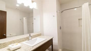 A modern bathroom with a granite countertop, a white sink, a large mirror, and a walk-in shower with a glass door.