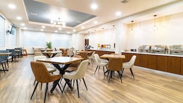 Un comedor moderno con suelo de madera, varias mesas y sillas, una encimera de cocina con dispensadores de alimentos e iluminación empotrada en el techo.