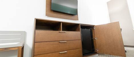 A bedroom with a wooden dresser, a television mounted above it, and a door leading to another room.