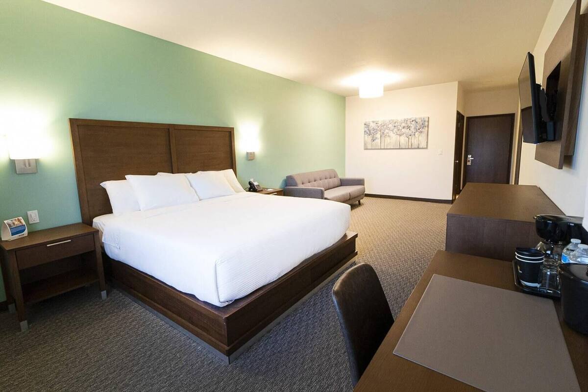 A hotel room with a large bed, a desk with a chair, a sofa, a coffee maker, and a painting on the wall.