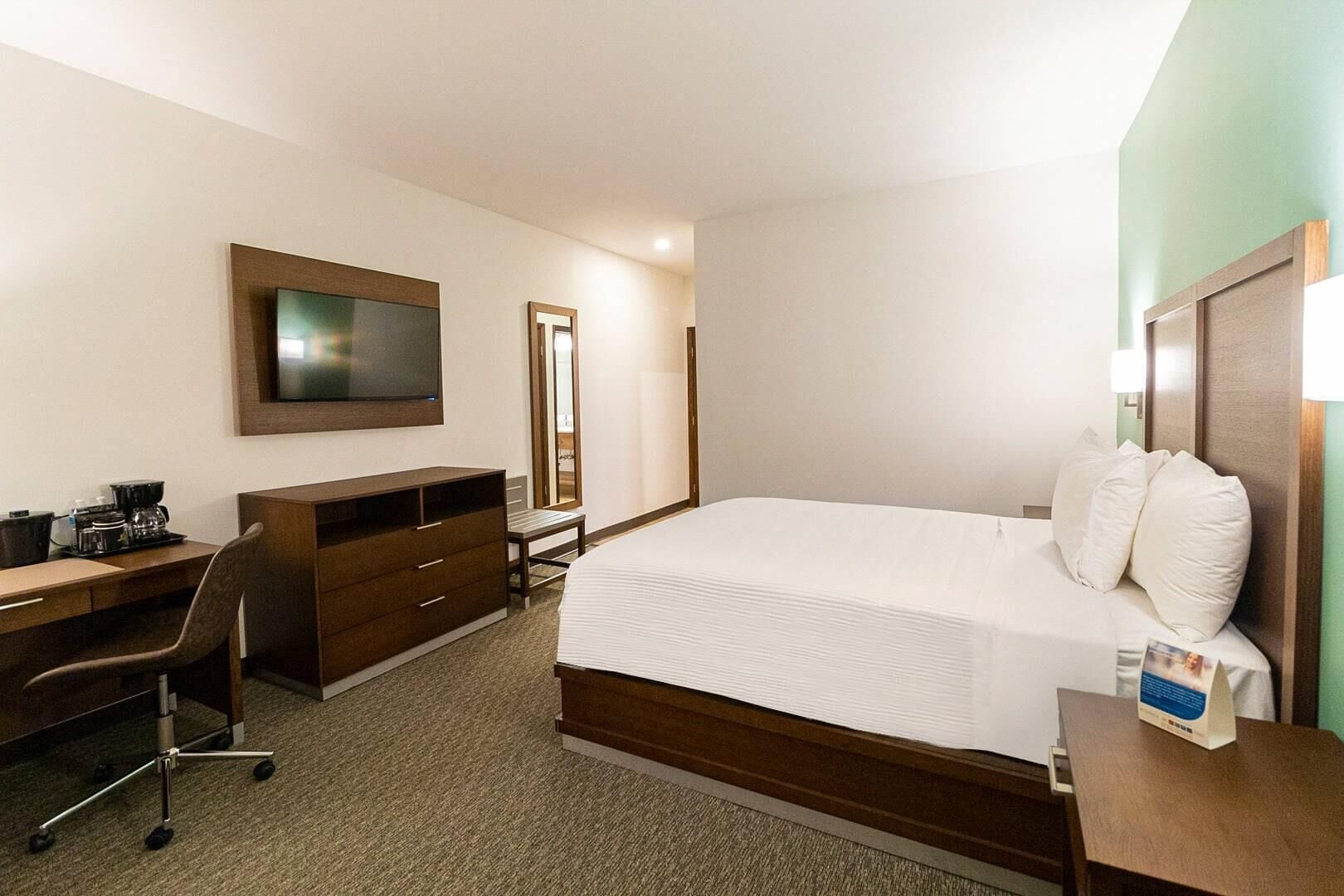 Una habitación de hotel con una cama, un escritorio, una silla, un televisor y un espejo.