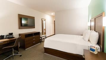Una habitación de hotel con una cama, un escritorio, una silla, un televisor y un espejo.