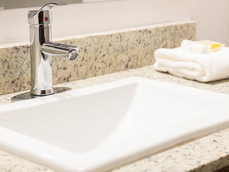 A white bathroom sink with a chrome faucet, a granite countertop, and a folded white towel with a yellow object on it.