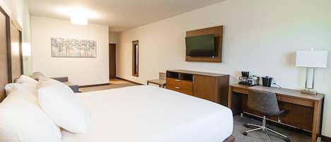 A hotel room with a large bed, a desk with a chair, a television, and a painting on the wall.