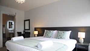 A hotel room with a large bed, two bedside tables with lamps, a mirror, and a door leading to a bathroom. - Number Two Dingle: Large Family Holiday Home (Dingle)