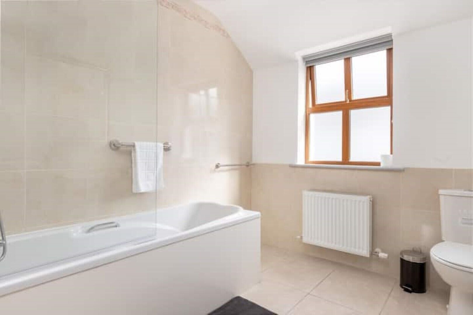 Une salle de bain avec une baignoire, une fenêtre, un radiateur et des toilettes.