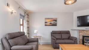Un salon avec deux canapés gris, une petite table, une lampe, une cheminée et un téléviseur fixé au mur.