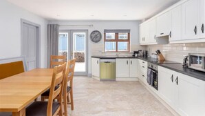 Une cuisine moderne avec des meubles blancs, un coin repas doté d’une table et de chaises en bois, et une vue sur l’extérieur grâce à une porte vitrée.