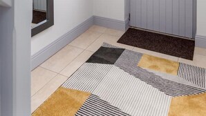 Un couloir avec une porte grise, un miroir et un tapis à motifs.